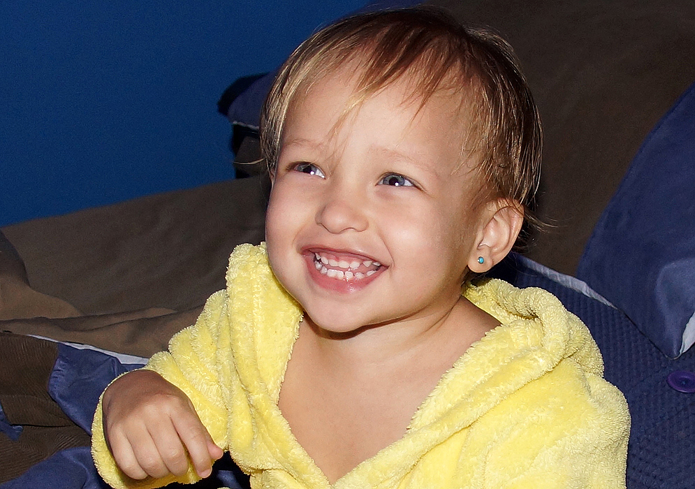 One-year-old girl with blonde hair and blue eyes smiling happily 