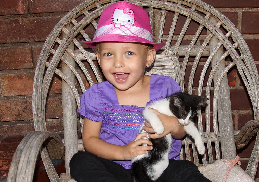 Happy one-year-old girl with blonde hair and blue eyes holding her cat