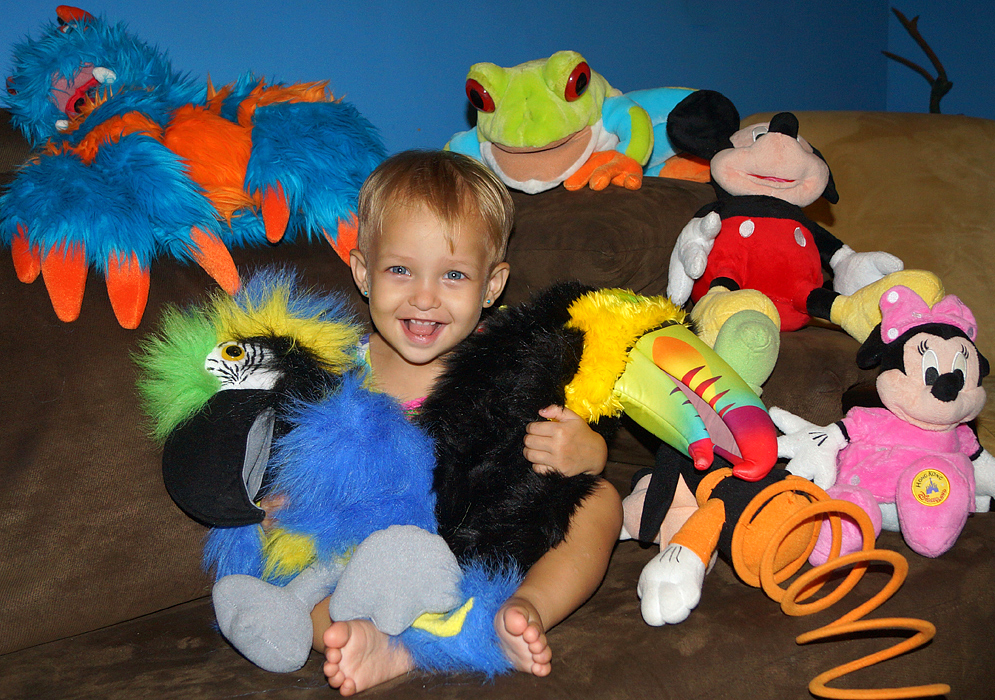Beautiful one-year-old girl with blonde hair and blue eyes surrounding by her stuff animals