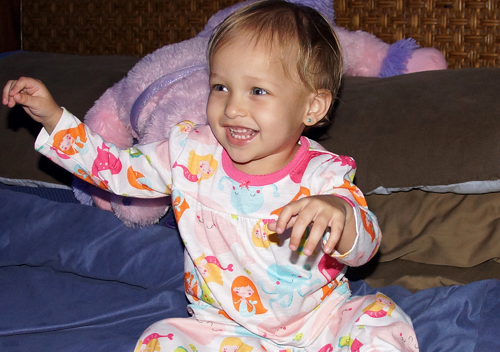 One-year-old girl with blonde hair and blue eyes in her pajamas in bed