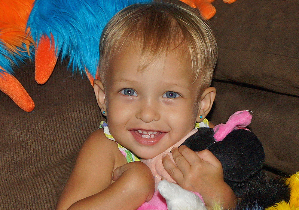 One-year-old girl with blonde hair and blue eyes holding stuff animal