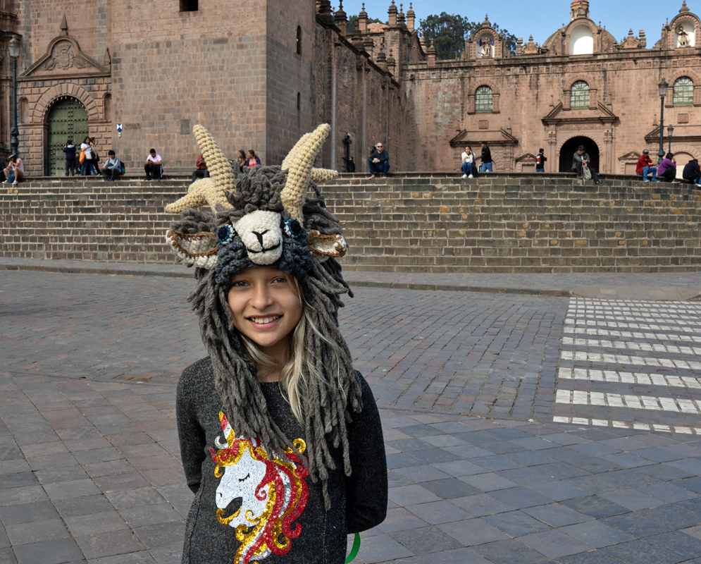Girl in Front of Cusco Cathedral. Girl wearing a unicorn sweater and Andean-style hat posing in front of the stone plaza and cathedral of Cusco, Peru