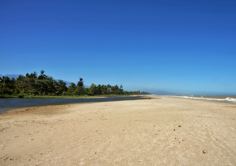 Large white beach with river, mountains and greenery and clear blue sky