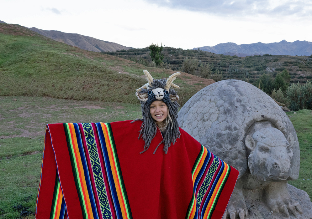 Girl with Giant Stone Armadillo Sculpture near Cusco Smiling girl in red poncho and animal hat posing beside a large sculpted stone armadillo in the highlands near Cusco, Peru