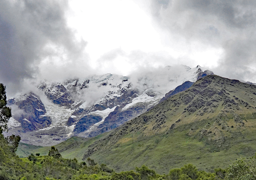 Glacier-Capped Peak Glacier-covered summit of Humantay rising dramatically behind a foreground of green ridges and misty clouds in the Peruvian Andes.