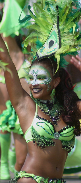 Carnival dancer in a bright green beaded costume and feathered headpiece raising her arm and smiling during the Barranquilla parade