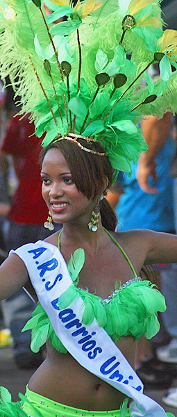 Carnival Queen in Green Feathered Costume oung Colombian woman wearing a green feathered headdress and costume with a sash labeled “A.R.S. Barrios Unidos,” dancing and smiling during the Barranquilla Carnival