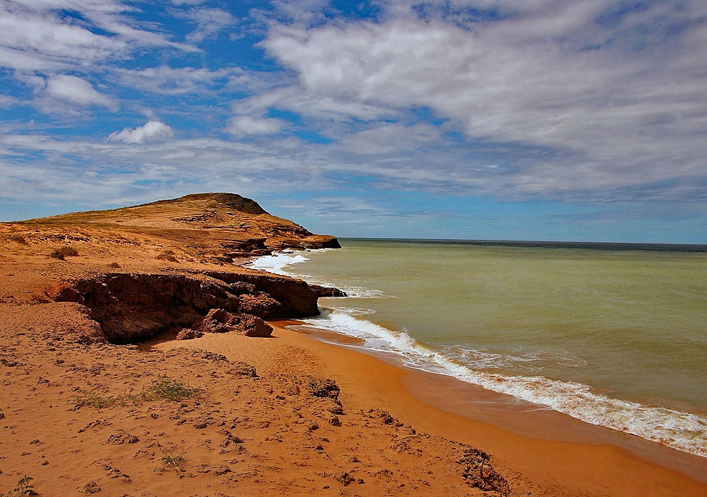 Guajira Desert Coastline Colombia Eroded orange desert cliffs and a narrow sandy beach meeting the green-blue Caribbean Sea beneath broken clouds
