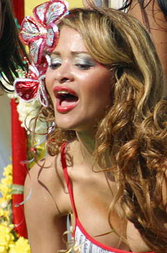 Smiling Colombian carnival woman with long wavy hair, wearing a festive outfit and sparkling red and silver floral headpiece, mid-celebration