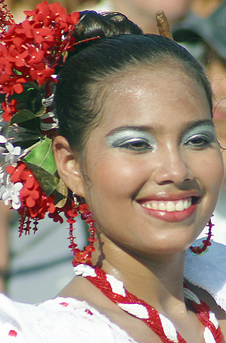 Smiling Colombian woman in traditional white dress with red accessories and silver eye makeup, adorned with red and white flowers during the Barranquilla Carnival