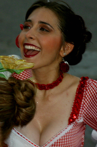 Laughing Colombian woman in red checkered traditional dress with sequins, wearing bold makeup and floral earrings during carnival celebration