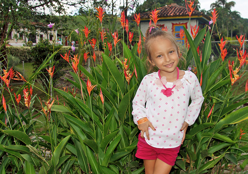 Pretty smiling blond five-year old wearing pink and white clothes in front of Heliconia psittacorum plants