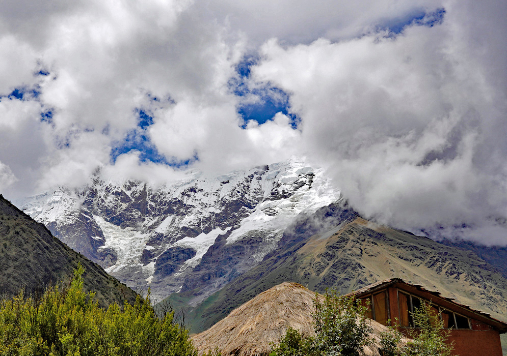 Humantay peak cloaked in glacial ice and swirling clouds, viewed from a nearby thatched-roof Humantay peak cloaked in glacial ice and swirling clouds, viewed from a nearby thatched-roof