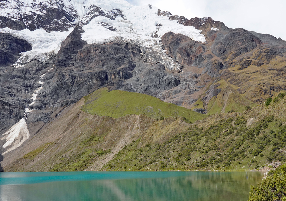 Humantay Lake Reflections Still turquoise waters of Humantay Lake reflect the surrounding steep rock walls and green slopes beneath snow-draped Andean cliffs