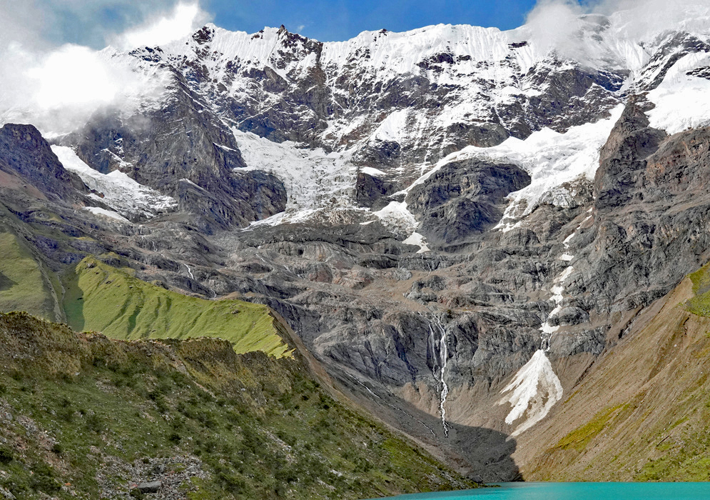 Humantay peak cloaked in glacial ice and swirling clouds, viewed from a nearby thatched-roof Humantay peak cloaked in glacial ice and swirling clouds, viewed from a nearby thatched-roof