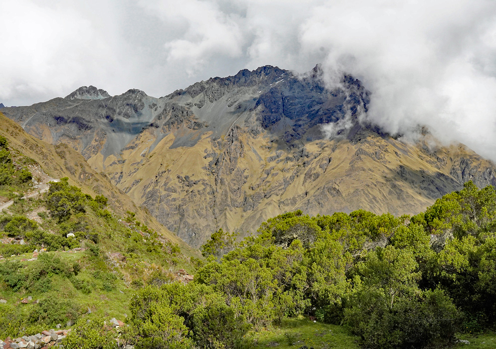 Humantay peak cloaked in glacial ice and swirling clouds, viewed from a nearby thatched-roof Humantay peak cloaked in glacial ice and swirling clouds, viewed from a nearby thatched-roof