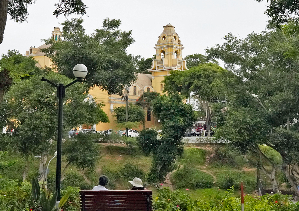 Iglesia La Ermita in Barranco, Lima The yellow colonial-style Iglesia La Ermita viewed through green trees and a park bench in Barranco, Lima