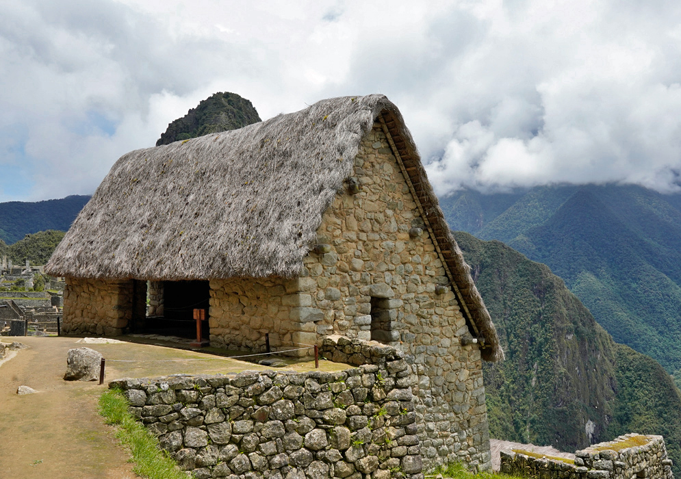 Machu Picchu Guardhouse Traditional thatched-roof stone guardhouse at Machu Picchu overlooking a misty landscape of Andean mountains