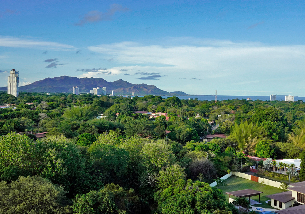 Nueva Gorgona Panama Ocean View Overlooking lush green vegetation and rooftops of Nueva Gorgona with tall apartment towers in the distance and the Pacific Ocean and rocky hills on the horizon