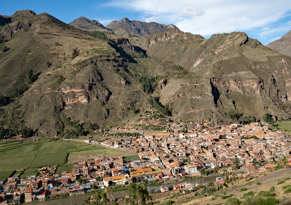 Aerial photo of the town of Ollantaytambo nestled below steep terraced mountains in the Sacred Valley of Peru, showing a dense grid of buildings and agricultural fields