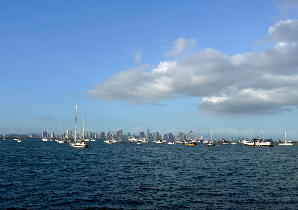 Pacific Bay View of Panama City Numerous anchored sailboats and yachts floating in the bay with a hazy view of Panama City’s skyline in the distance under a partly cloudy sky