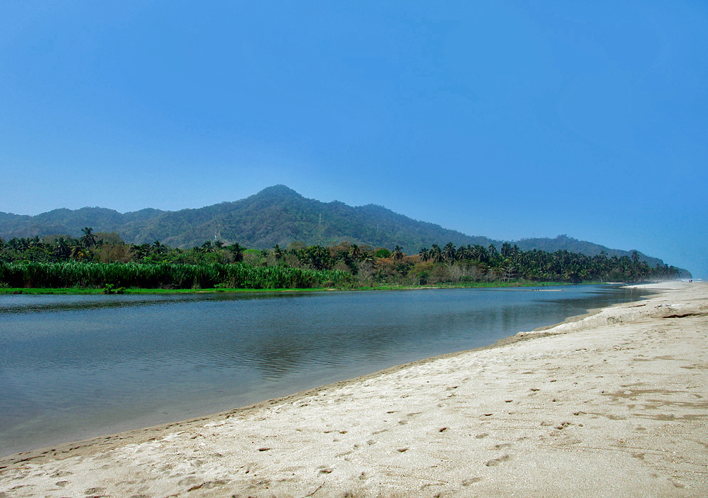 Palomino River with green vegetation and a mountain on one shore line and white sand on the other shoreline