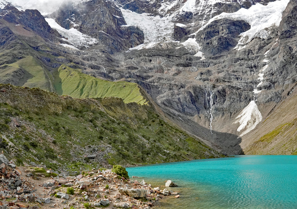 Humantay Lake Glacial Scenery A turquoise glacial lake known as Humantay Lake at the base of snow-capped Andean mountains, surrounded by rocky slopes and high-altitude vegetation under a partially cloudy sky