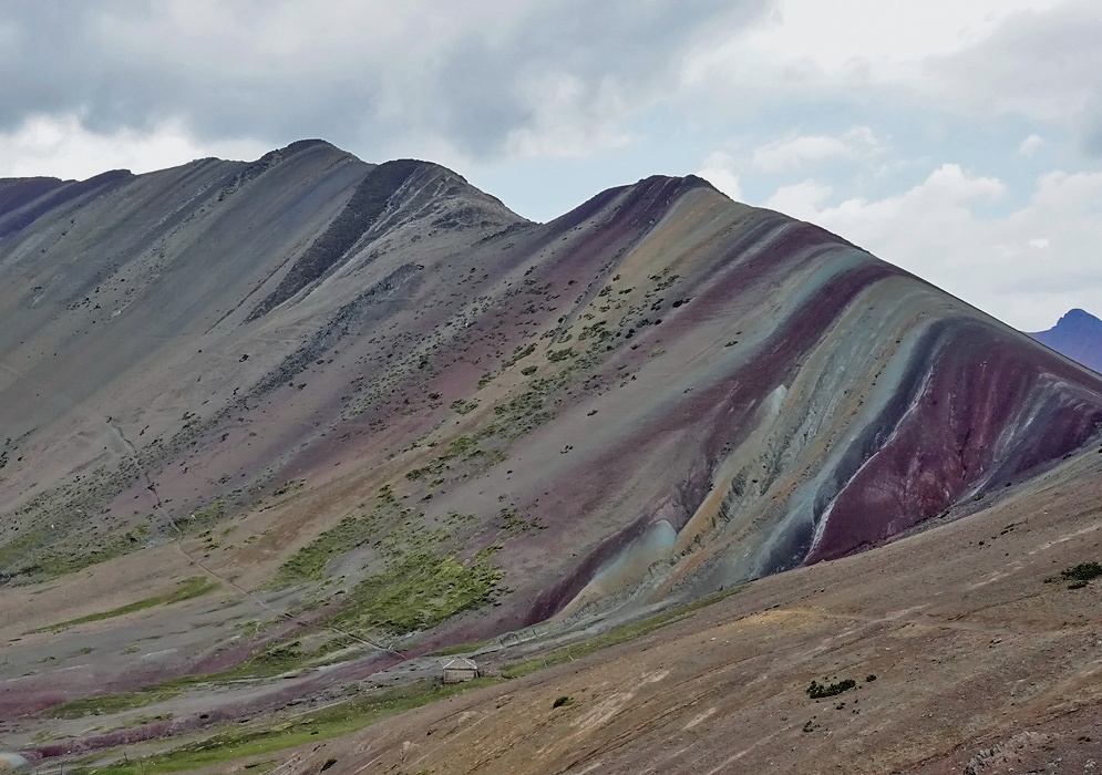 Alternative Rainbow Mountain Peru Sloped Andean ridge in Peru painted with wide, multicolored stripes of maroon, teal, and sandy yellow caused by natural mineral deposits