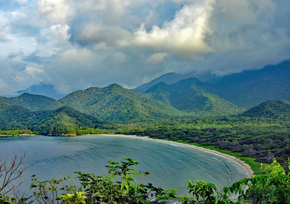 Full vista of curving beach with green mountains and clouds