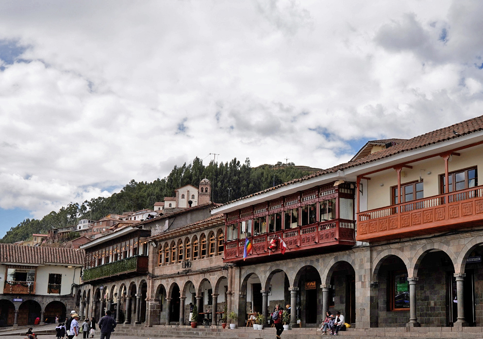 Colonial Architecture and Hillside Backdrop in Cusco Traditional Cusco buildings with red balconies and arched porticos, backed by hills and a white church on the mountainside