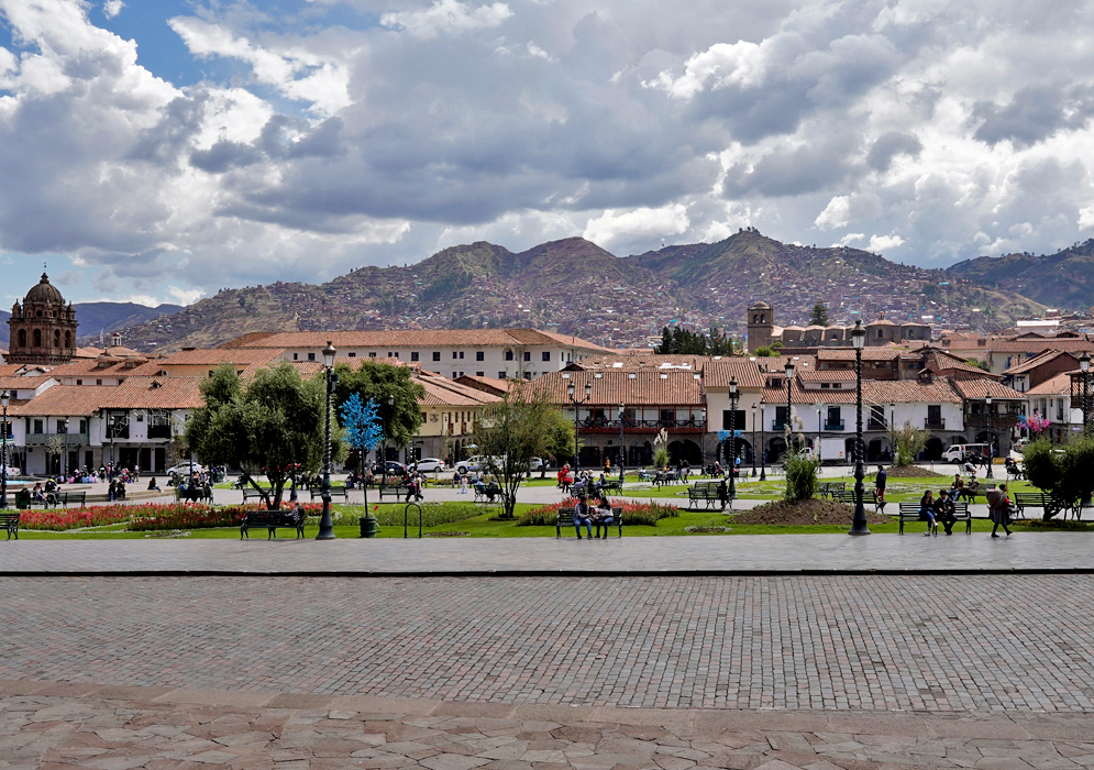 Plaza de Armas Peru Panoramic view of Cusco’s Plaza de Armas with colonial buildings, tree-lined walkways, and the Andes Mountains in the distance