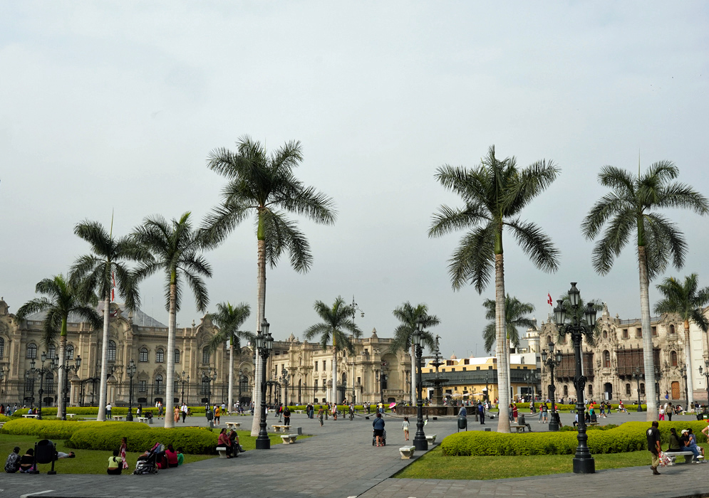 Plaza Mayor de Lima Historic Plaza Mayor de Lima with tall palm trees, colonial-era buildings, and people walking and relaxing in the central green square.