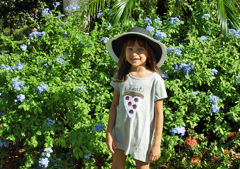 Pretty girl with a hat standing in front of a Plumbago auriculata bush