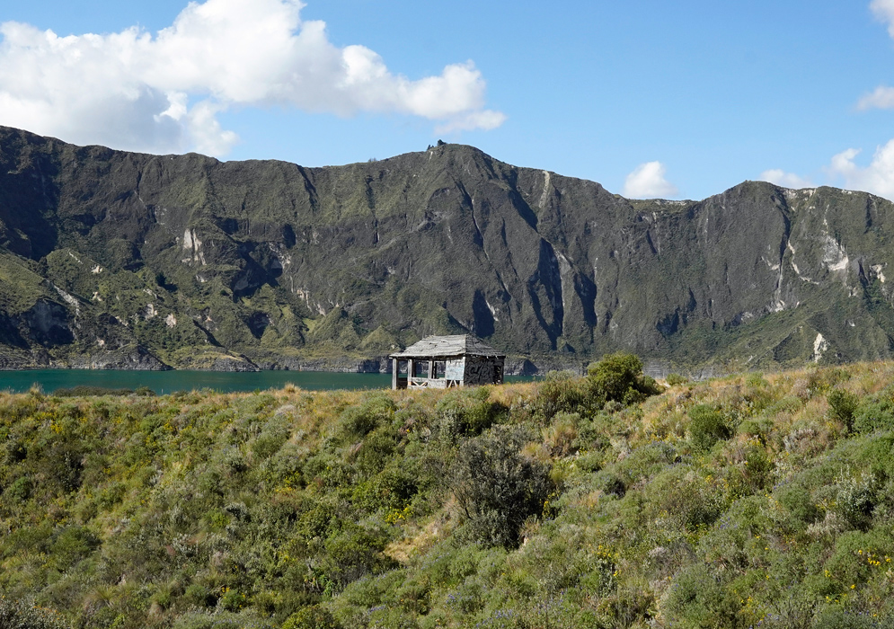 Quilotoa Crater Shelter A weathered wooden shelter stands alone on the grassy rim of Quilotoa Crater, with steep volcanic cliffs and the emerald lake in the background