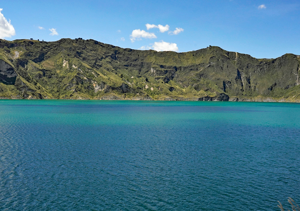 Quilotoa Lake From Below Deep blue and green hues of Quilotoa Lake shimmering below the jagged crater rim on a sunny day