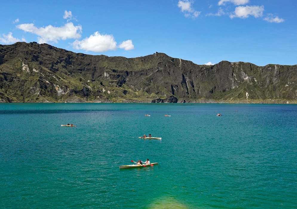 Quilotoa Lake Boats Visitors rowing boats across the turquoise waters of Quilotoa Lake with dark rocky cliffs in the background