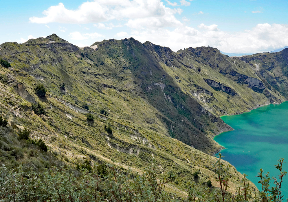 Quilotoa Lake Rim Steep green slopes of the Quilotoa crater rim leading down to the curved shoreline of the lake below