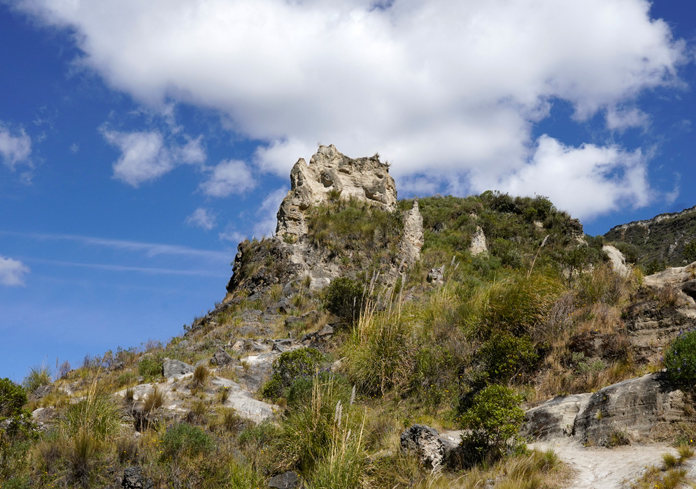 Quilotoa Crater Trail Jagged volcanic rock formation rising above dry grass and shrubs on the rugged trail near the rim of Quilotoa crater in Ecuador