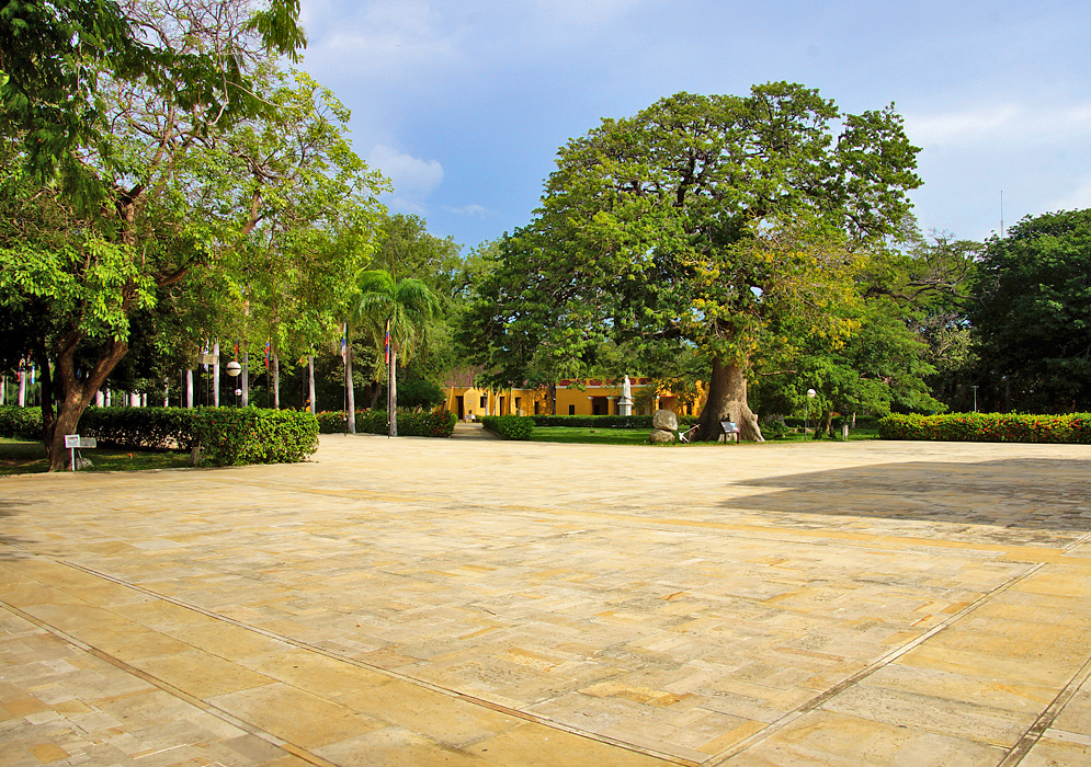 A large stone-colored courtyard with flags and yellow buildings in the background