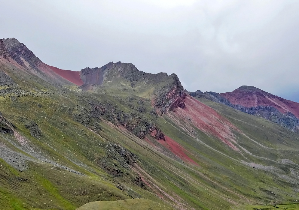 Expansive Andean landscape with a series of mountains vividly striped in red, pink, and green tones, showcasing the geological beauty of the Rainbow Mountains in Peru
