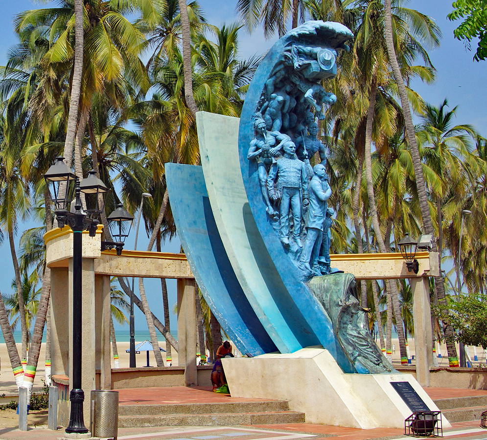 A blue statue representing historical figures of La Guajira with beach, ocean and palm trees in the background