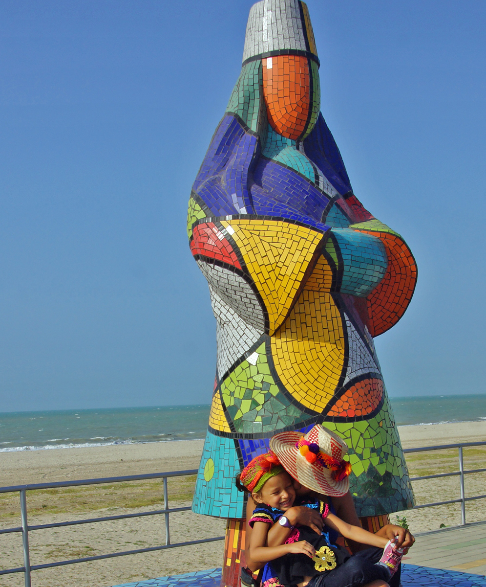 Colombian mom hugging her happy young daughter in front of a colorful tile statue honoring the Wayuu indians