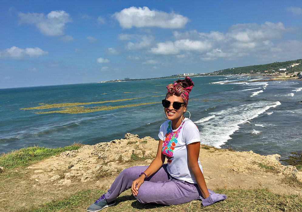 An attractive Colombian woman sitting on a cliff overlooking the ocean near Barranquilla on a clear sunny day
