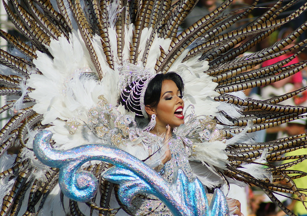 Stunning Colombian carnival queen in a lavish silver costume with radiant feathers and a sparkling crown, passionately performing during the Barranquilla Carnival parade