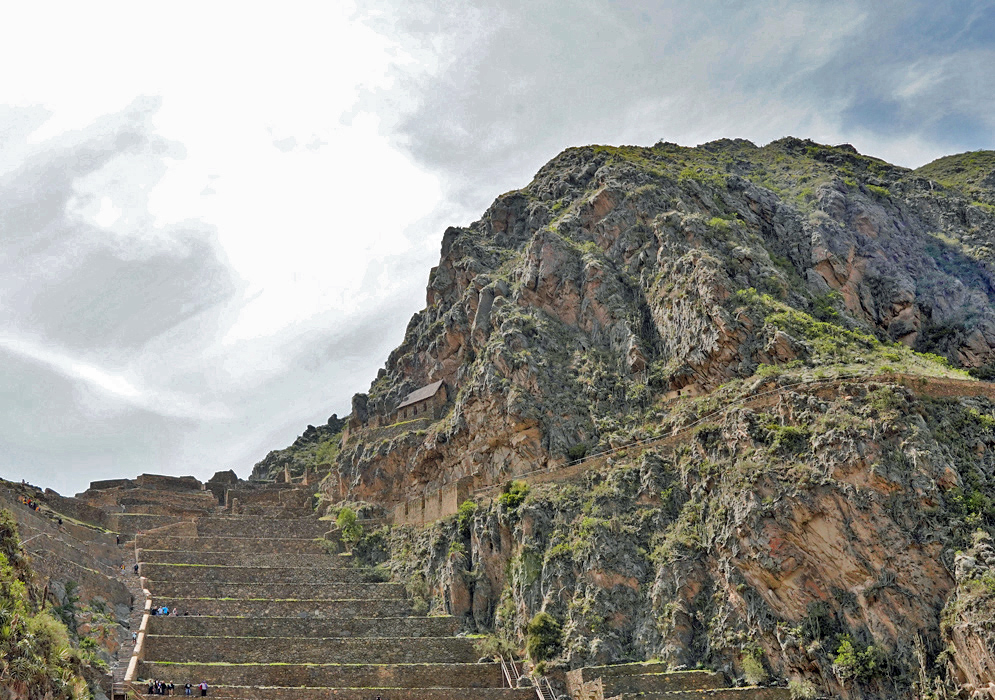 Ollantaytambo Agricultural Terraces Steep agricultural terraces of Ollantaytambo climbing a dramatic mountain slope with visitors walking along stone steps and a small thatched hut above