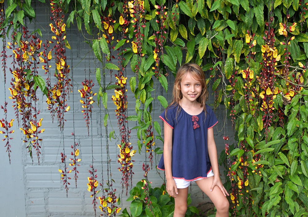 Beautiful young eight year old girl in front of a Thunbergia mysorensis flowering vine