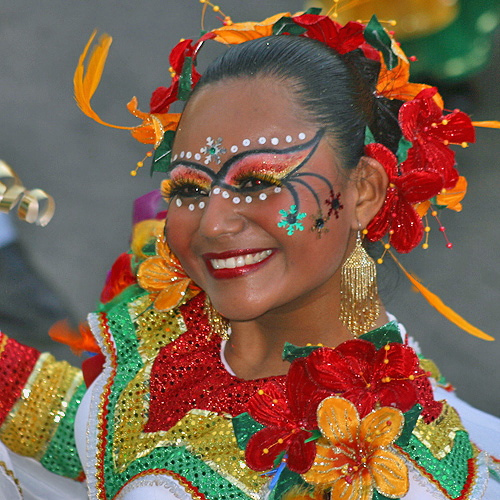 Joyful Colombian dancer in traditional red, yellow, and green costume with floral headpiece and detailed face paint during Barranquilla Carnival