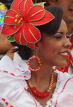 Smiling Barranquilla Carnival Performer in Red and White Woman wearing a traditional red and white carnival outfit, with a large red flower headpiece and festive beaded jewelry, smiling during the Barranquilla parade