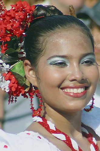 Smiling Colombian woman in traditional white dress with red accessories and silver eye makeup, adorned with red and white flowers during the Barranquilla Carnival