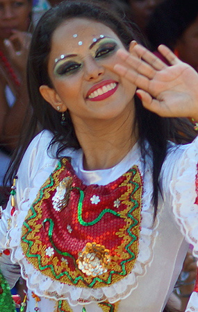 Carnival Performer Waving in Traditional Dress Cheerful woman with festive face paint and vibrant eye makeup, waving and smiling in a traditional white and red embroidered costume during the Barranquilla Carnival